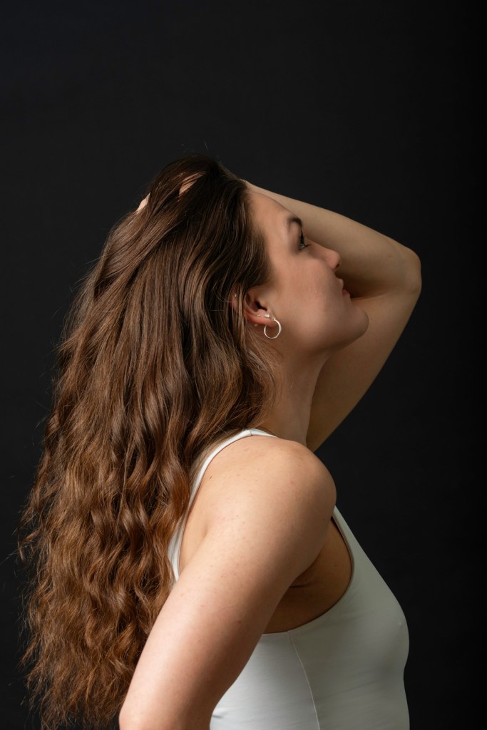 Woman stands facing the side running her hands through her hair.  studio photography.