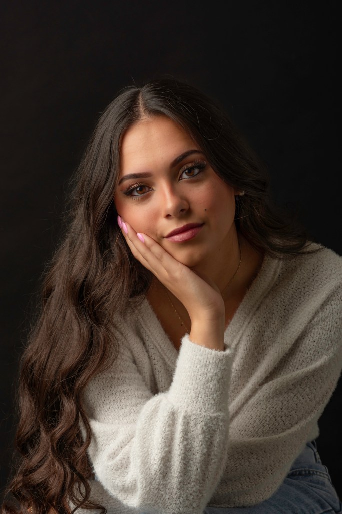 woman in white sweater rest her head on her hand. studio photography.