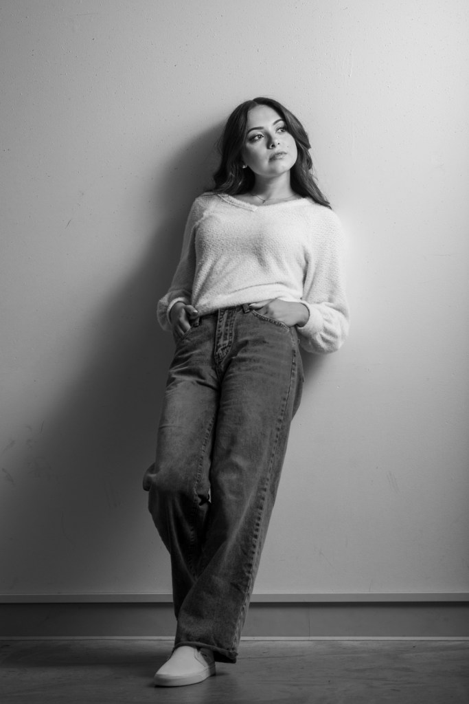Young woman leans on wall and poses with hands in her pockets. studio photography.