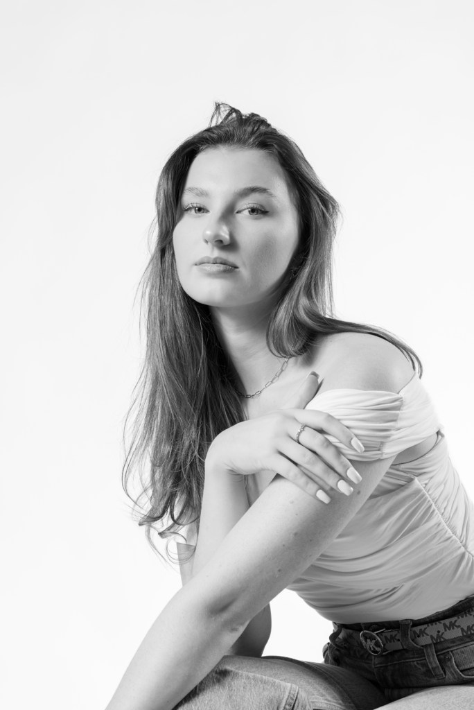 woman in a white shirt leans and grabs her arm. studio photography.