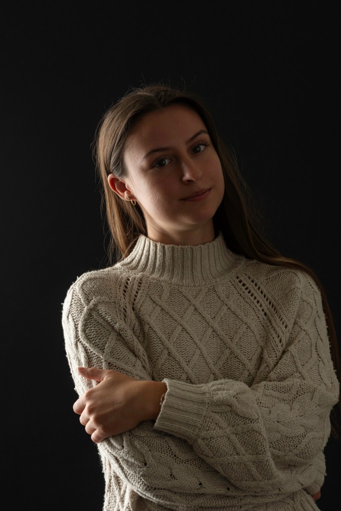 woman stands with head tilted and arms crossed. studio photography.