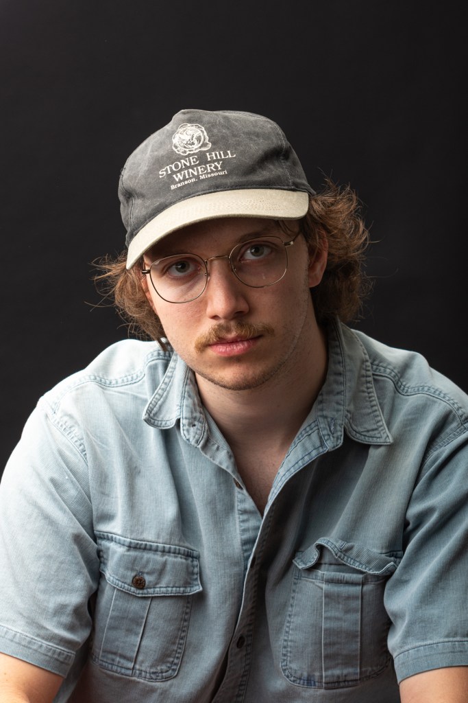 Man with hat, glasses, and blue shirt poses. studio photography.