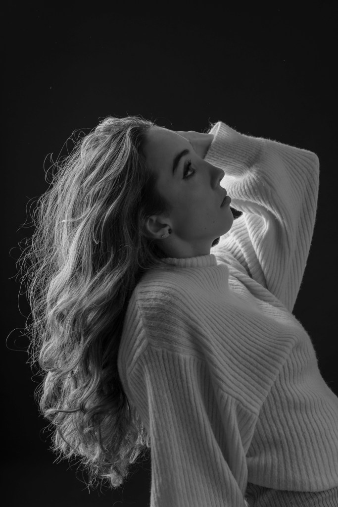 woman leans back and runs hand through her hair. studio photography.