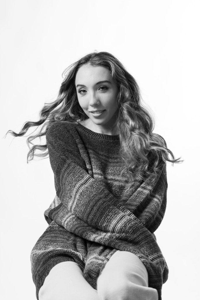 Woman in sweater crosses her arms around her body with her hair flowing. studio photography.