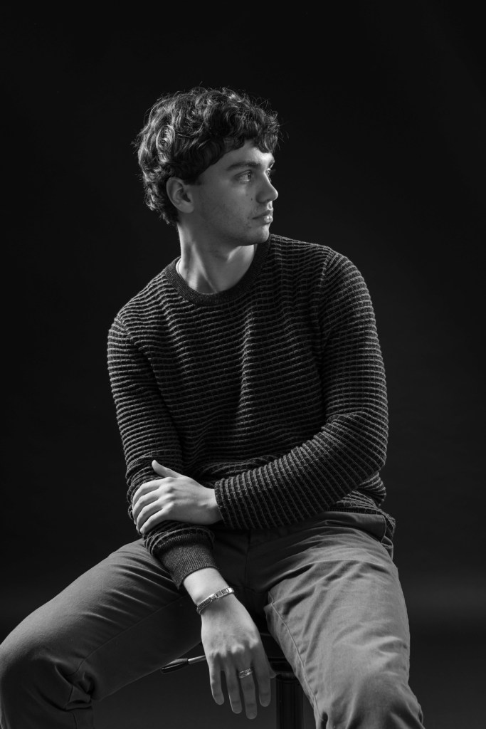 young man poses in a studio with black background.