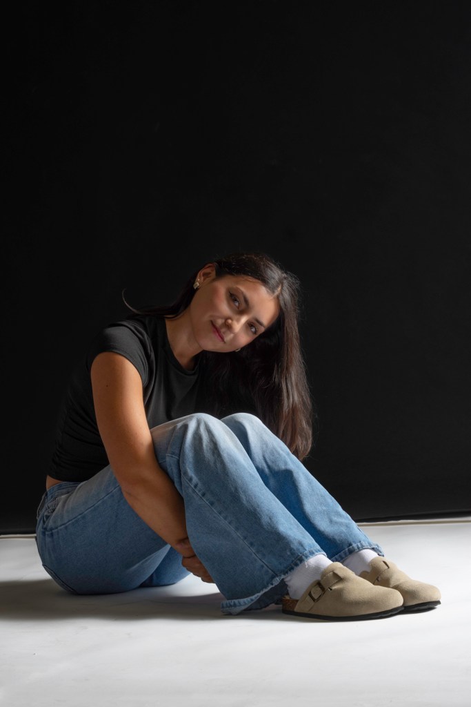 Woman sits and wraps her arms around her legs. studio photography.