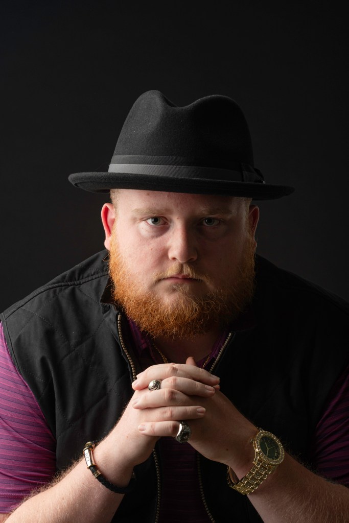 Young man with beard poses with hands under his chin. studio photography.