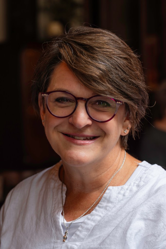 Middle age woman in a white shirt smiles.