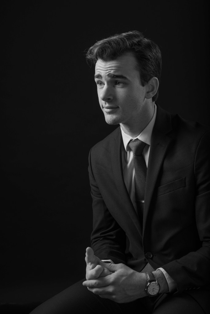 Young man in a suite and tie sits and looks left. studio photography.