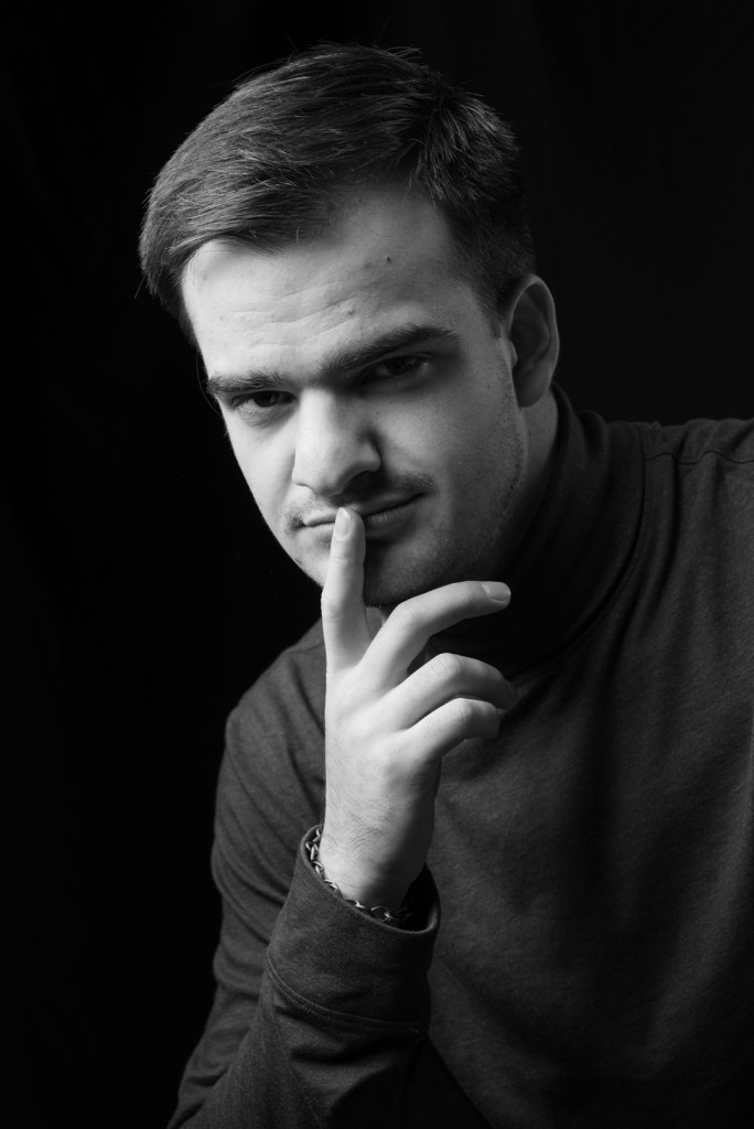 man in a turtleneck sweater holds finger to his mouth. studio photography.