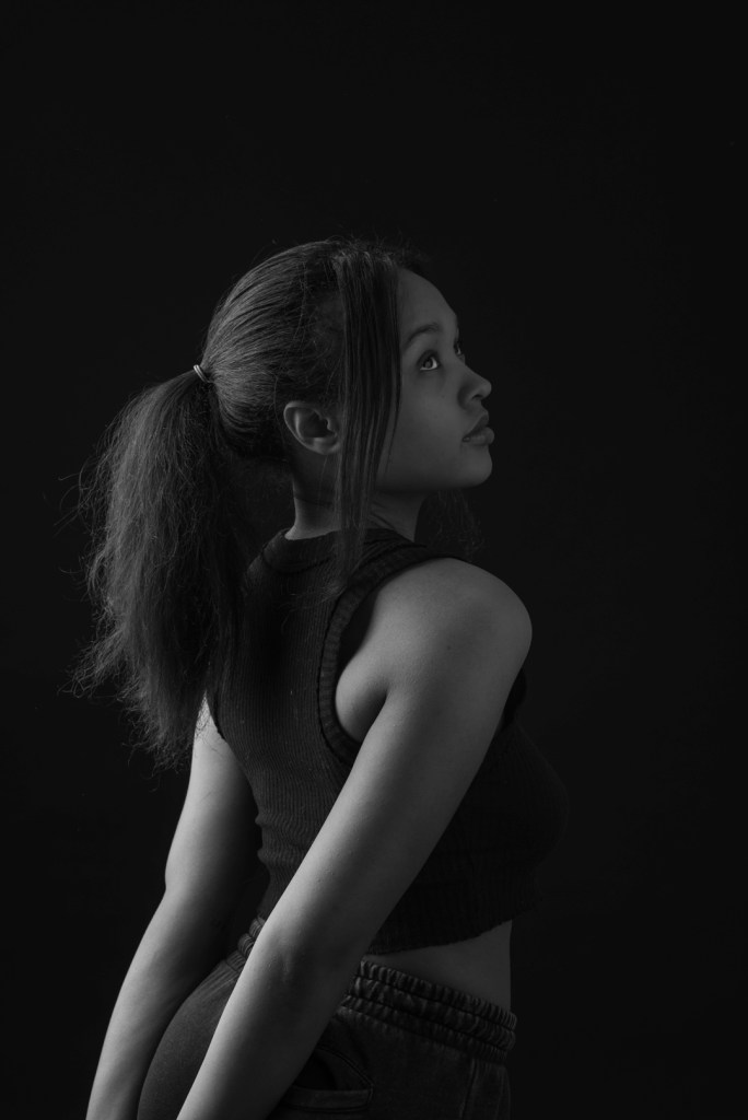 woman clasps her hands behind her back and looks to the right. studio photography.